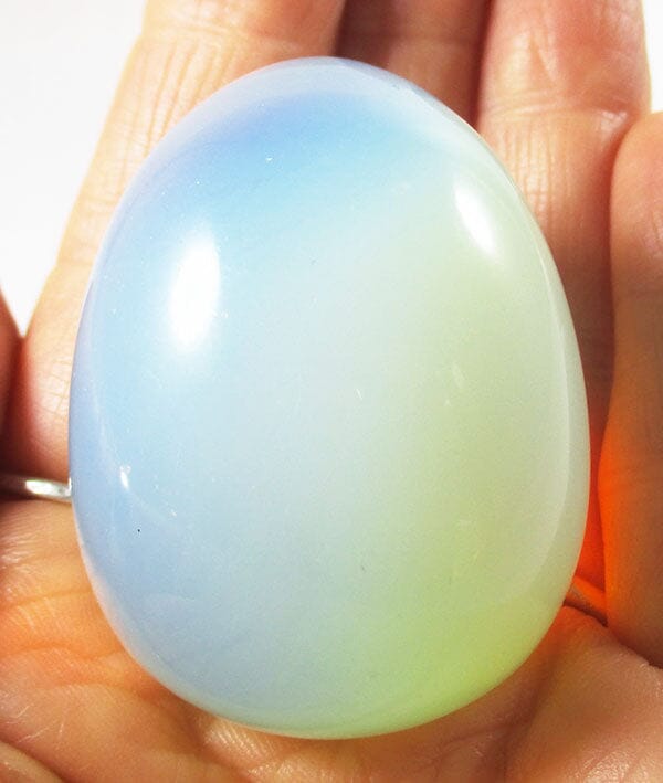 A blue/white carved crystal opalite egg held in the palm of the hand